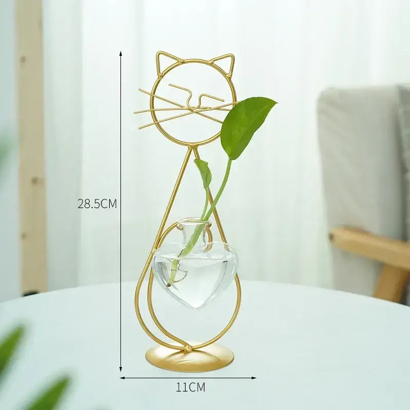 Gold-toned metal vase shaped like a cat with a clear glass heart container and single green leaf for home decor