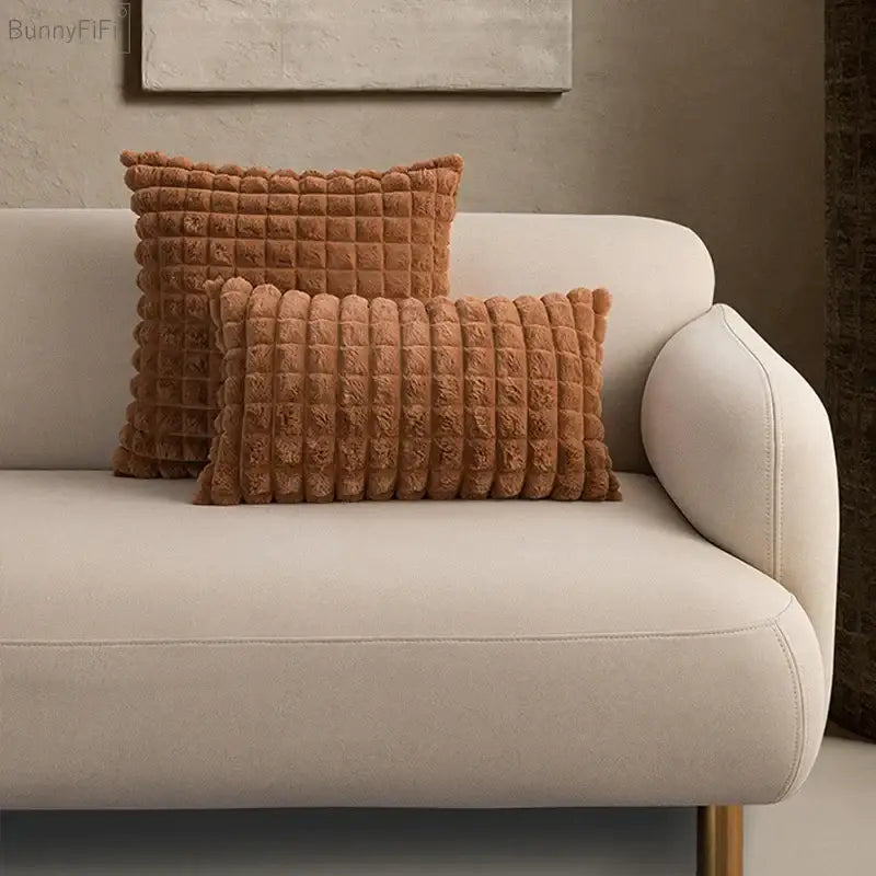 Two rust-colored decorbites fluffy faux fur cushion covers with plush quilted texture on a beige sofa