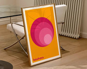 A framed geometric canvas poster with concentric pink circles on orange background in a light wood frame