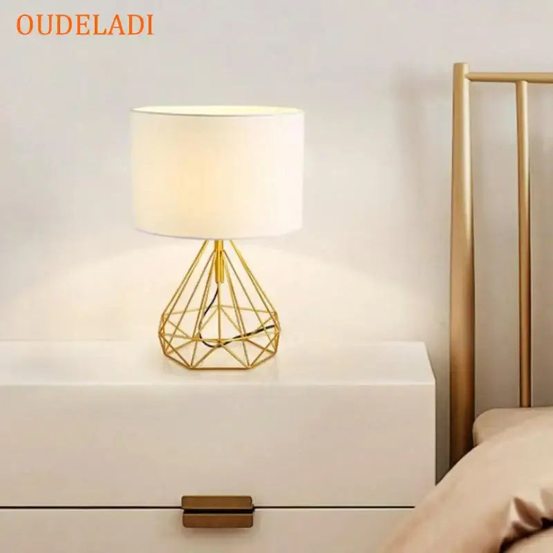 Decorbites geometric gold desk lamp with a gold wireframe base and white cylindrical shade for bedroom tables