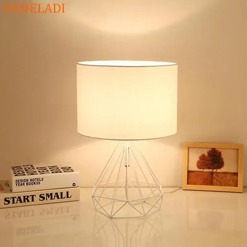 Decorbites geometric gold desk lamp with white cylindrical shade and wireframe base casting warm light for bedroom use