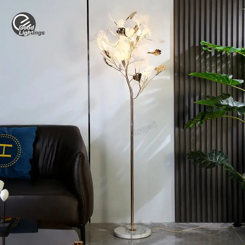 Tall slender decorbites ginkgo leaf floor lamp with gold metal stem and white flower-shaped led lights for living room