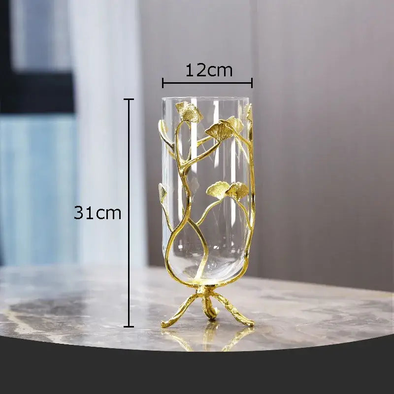 A tall clear glass vase with a golden ginkgo leaf metal frame on three ornate legs by decorbites ginkgo leaf collection