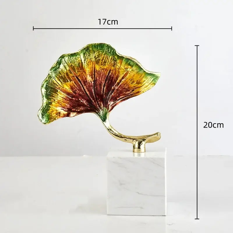 Decorbites ginkgo leaf metal sculpture with vibrant green yellow and red hues on a gold stem and white marble base