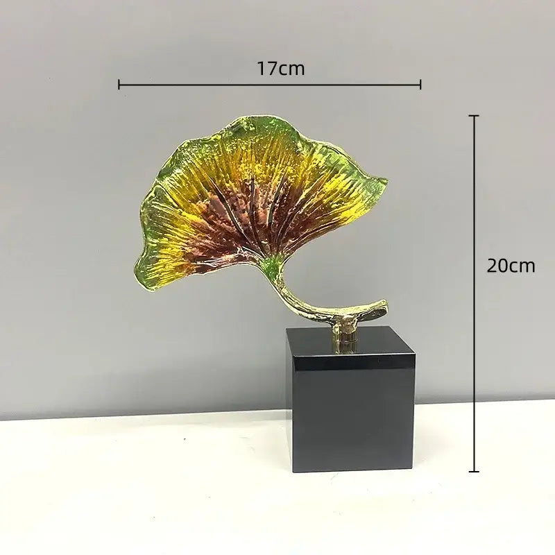 A vibrant decorbites ginkgo leaf metal sculpture with glossy green to brown hues on a sleek black base for home decor