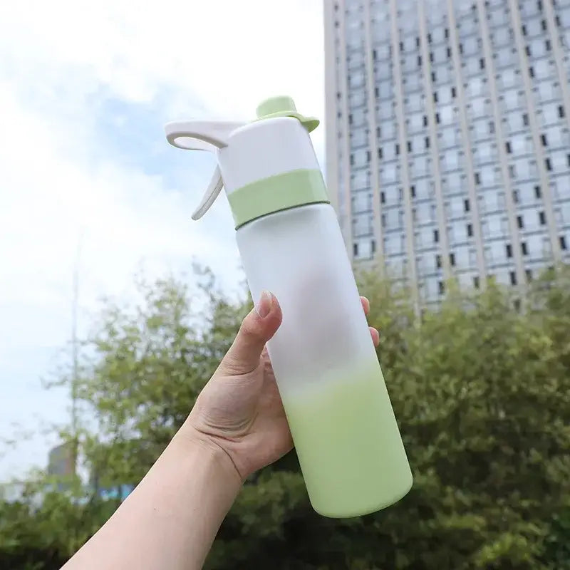 A translucent light green decorbites girls spray water bottle with white and mint green nozzle held against urban background