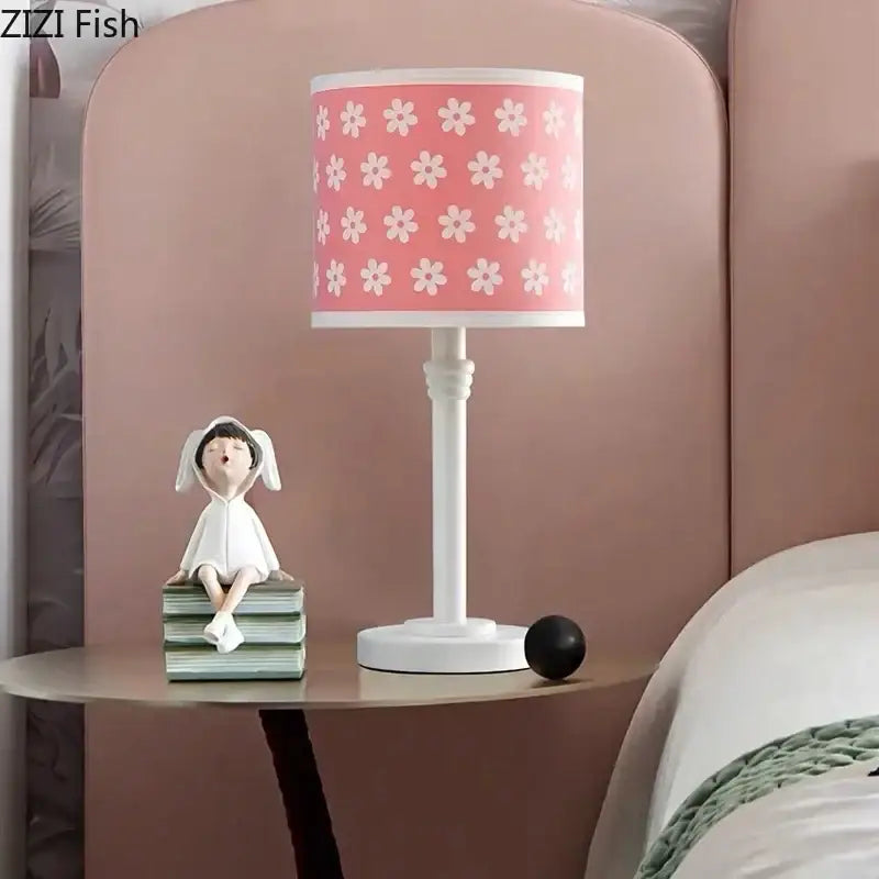A pink lampshade with white floral patterns on a white lamp base complements the DecorBites™ books resin sculpture figure