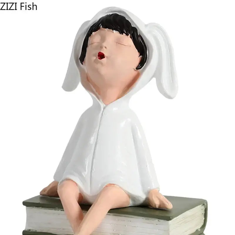 DecorBites™ resin sculpture figure of a white bunny-hooded girl with black hair and red lips sitting atop a book