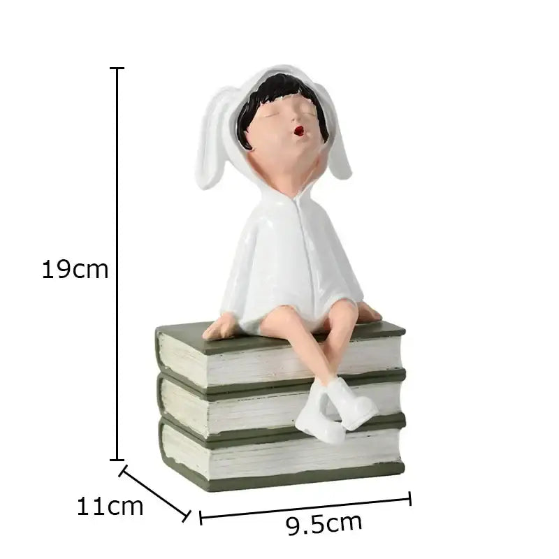 White bunny-eared resin sculpture figure sitting atop a stack of books for modern room decor by DecorBites™
