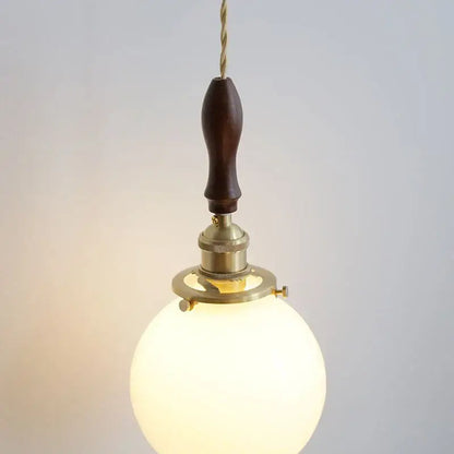 A warm spherical glass pendant lamp with walnut wood handle and brass hardware decorbites glabe led pendant