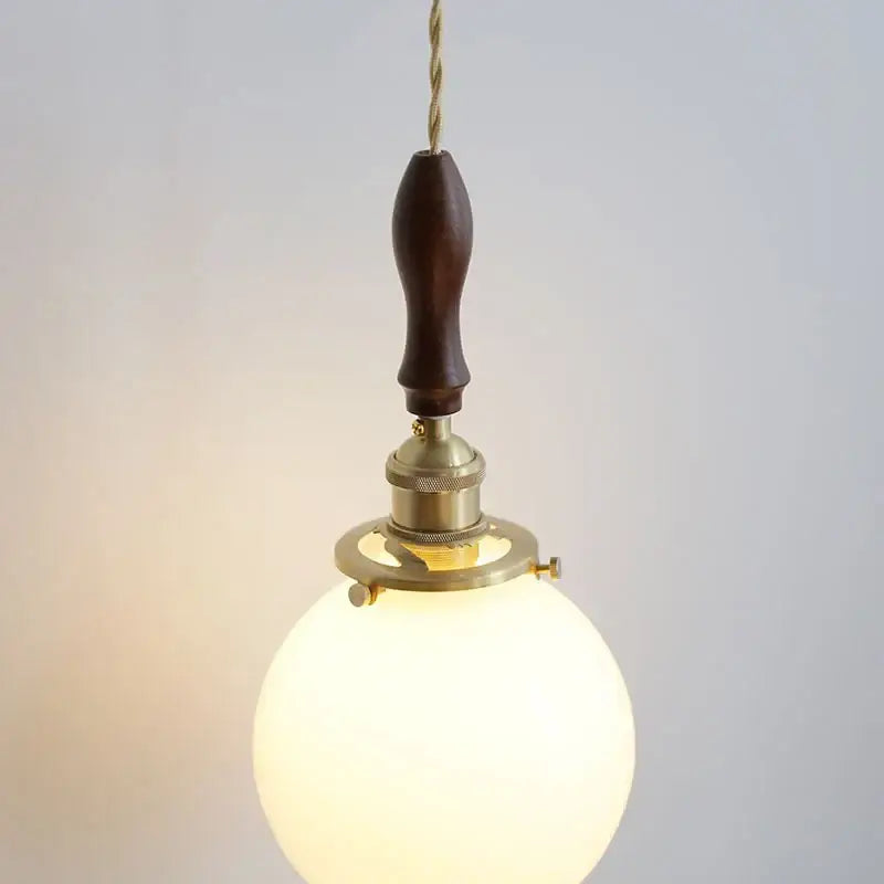 A warm spherical glass pendant lamp with walnut wood handle and brass hardware decorbites glabe led pendant