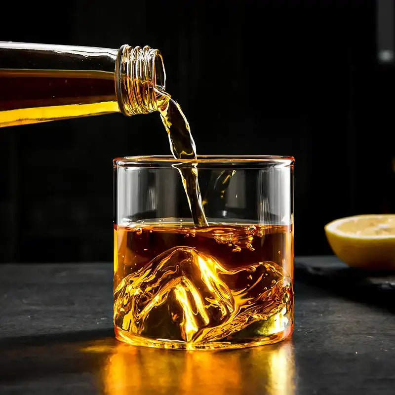A clear glass decorbites glacier wine cup with sculpted mountain base filled with amber whisky liquid