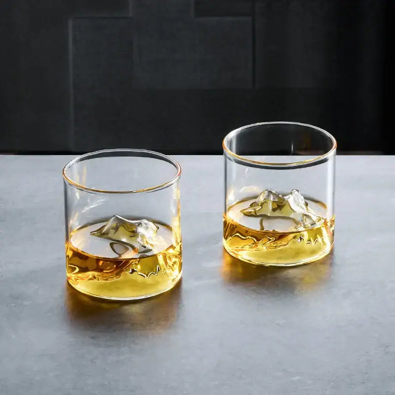 Clear glass decorbites glacier wine cup with gold rims containing amber liquid and ice cube for whisky use