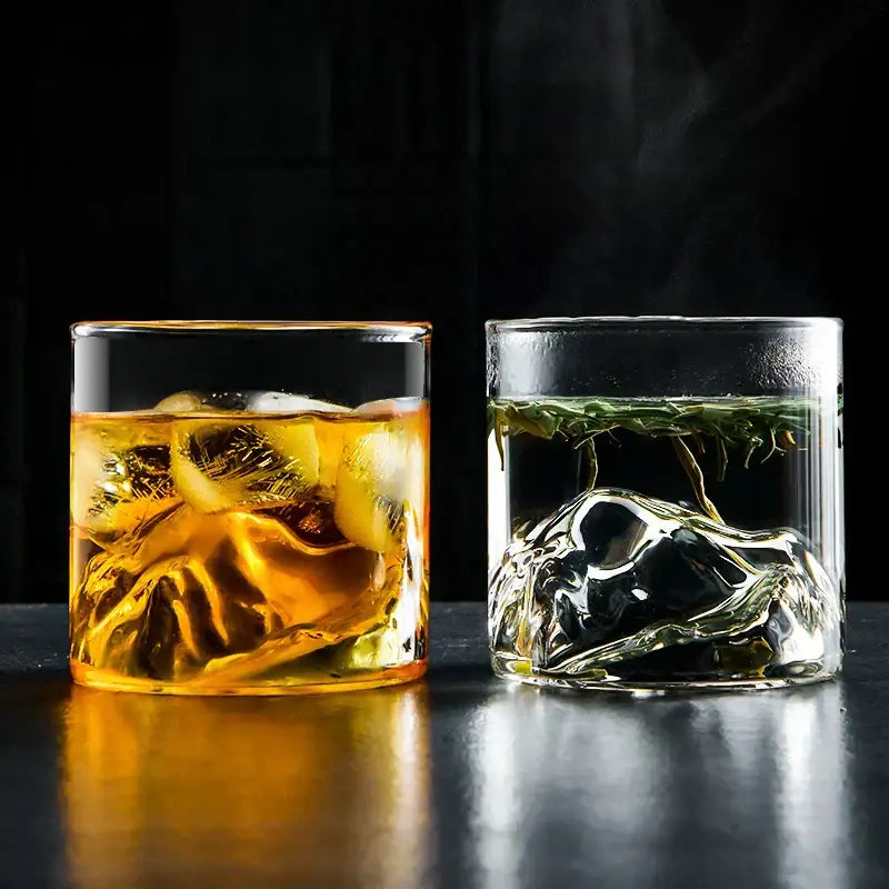 Two clear glass decorbites glacier wine cups with amber whiskey and green tea showcasing Japanese style and Fuji artwork