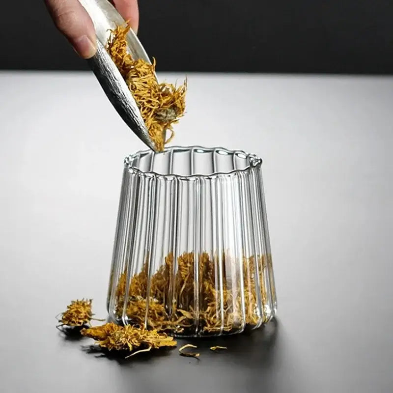 Clear glass vase with vertical ridges and fluted rim holding dried yellow flowers in decorbites glass airtight canister with wooden lid