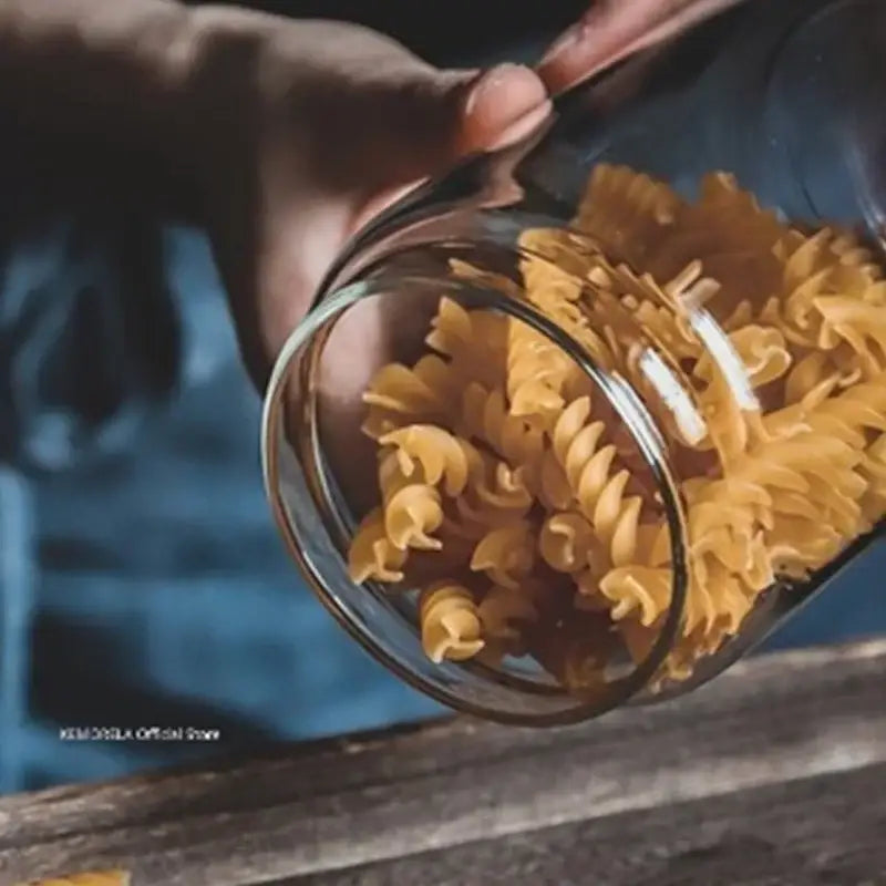 A clear glass airtight canister from decorbites filled with golden-yellow spiral pasta with a wooden lid