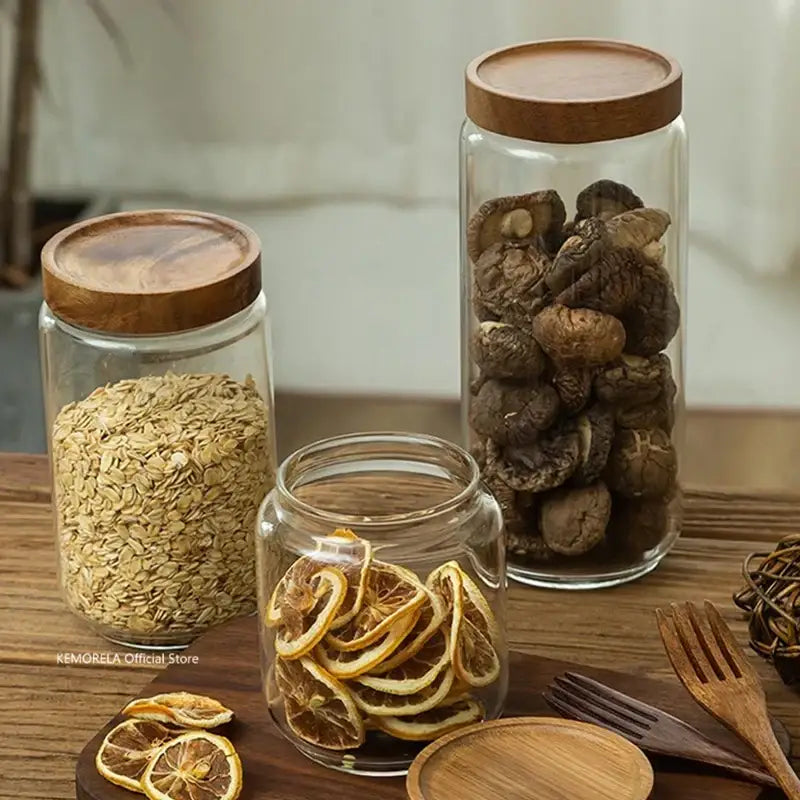 Three clear decorbites glass airtight canisters with wooden lids containing oats mushrooms and sliced citrus for kitchen storage