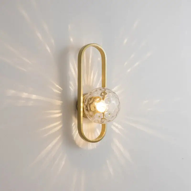 Gold-toned decorbites glass aisle wall lamp with textured clear glass globe emitting warm light for indoor decor