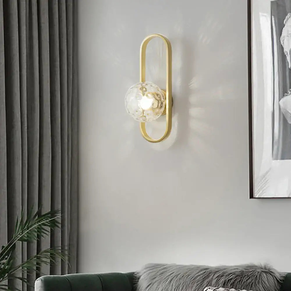 Gold-toned decorbites glass aisle wall lamp features a textured clear glass globe for post-modern indoor lighting
