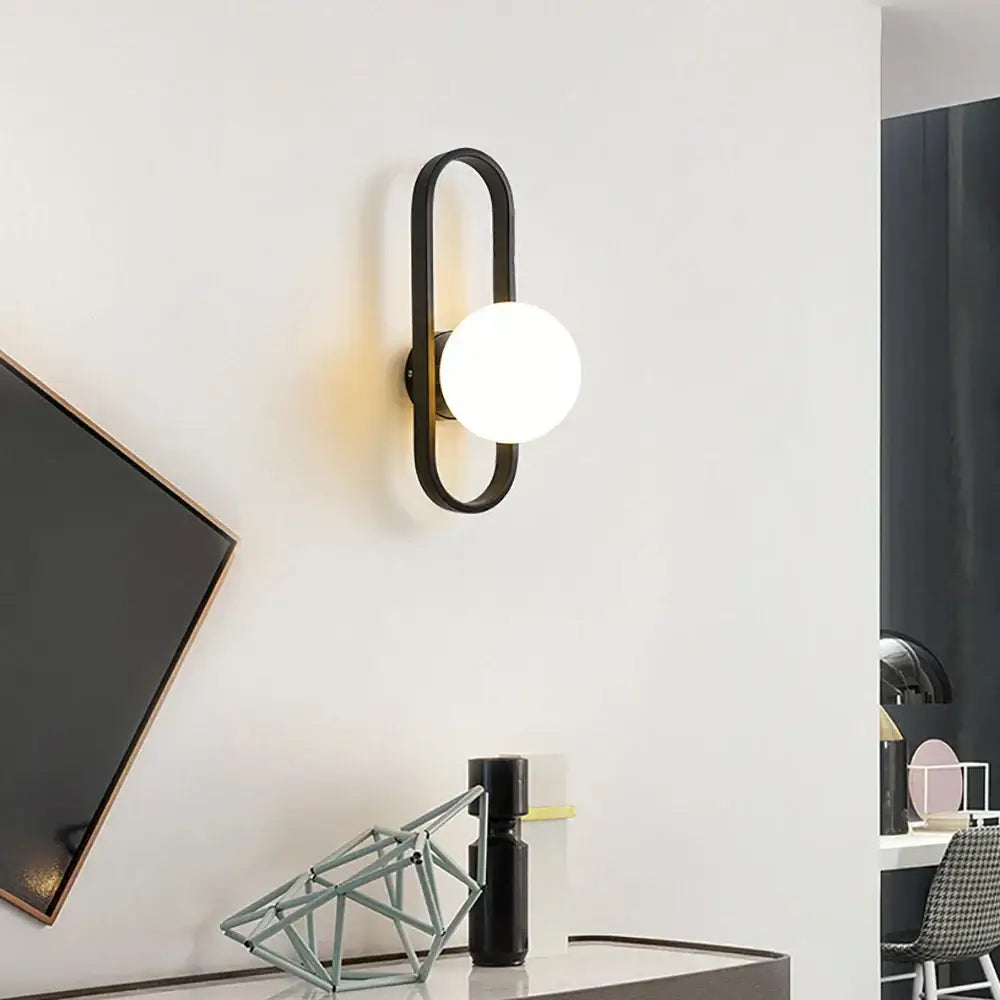 Black metal DecorBites glass aisle wall lamp with sleek curved frame and round frosted glass bulb for indoor decoration