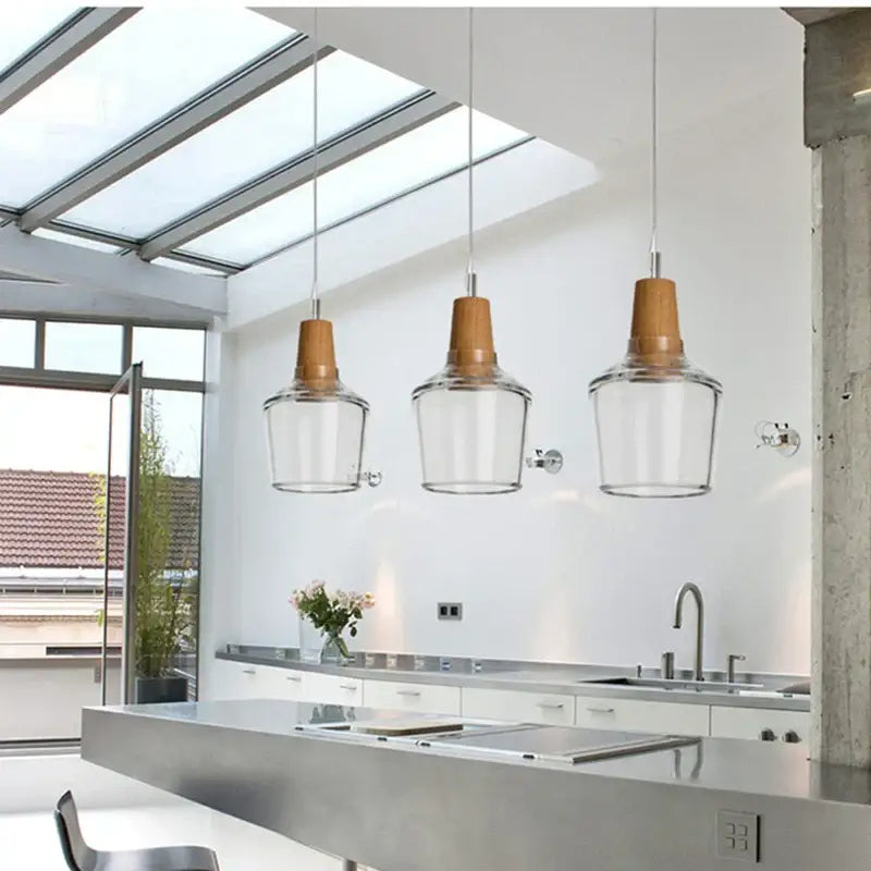 Three modern DecorBites glass and wood pendant lights with clear shades and warm wood tops for dining loft decor