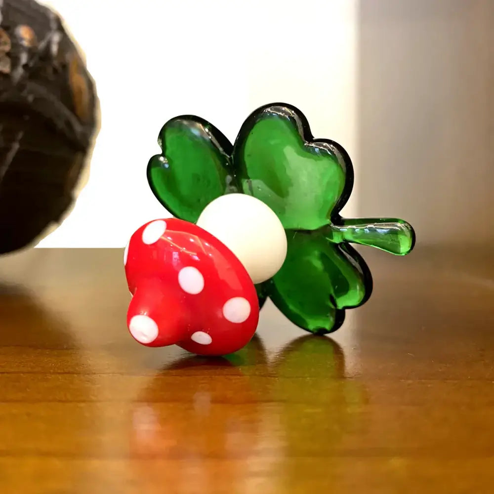 A glossy red glass animal figurine mushroom with white polka dots and a green four-leaf clover base for decor
