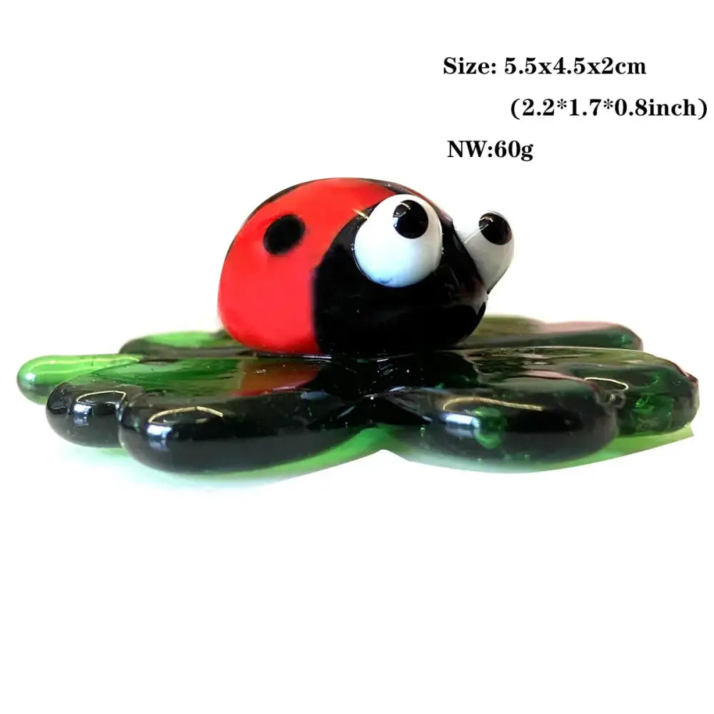 A glossy red and black glass animal ladybug figurine with large white eyes on a green leaf-shaped base for decorbites