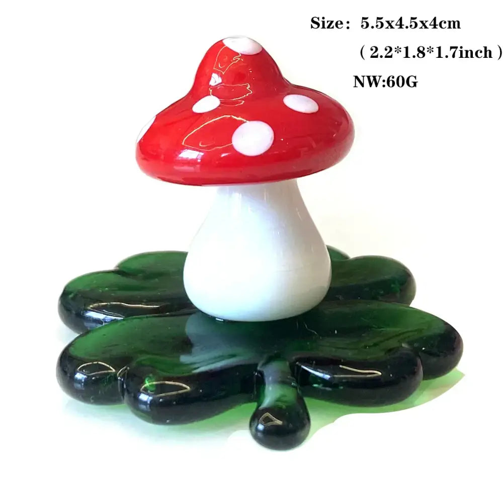 A glossy red and white mushroom glass animal figurine with white spots on a dark green leaf base from DecorBites