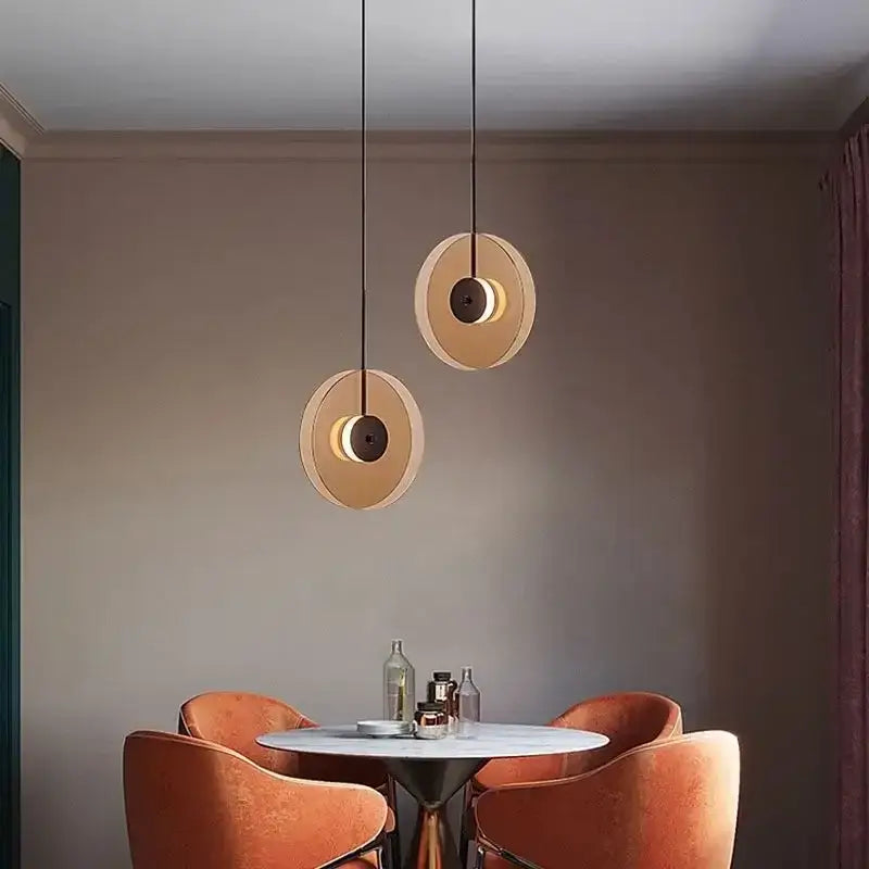 Two modern decorbites glass art chandelier pendant lights with warm circular glass shades and dark metal accents hang above table
