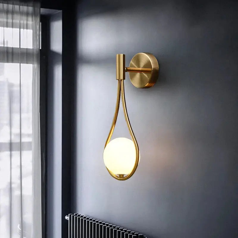 Gold-toned decorbites glass ball brass wall lamp with teardrop frame and warm-glowing LED bulb for bedroom lighting