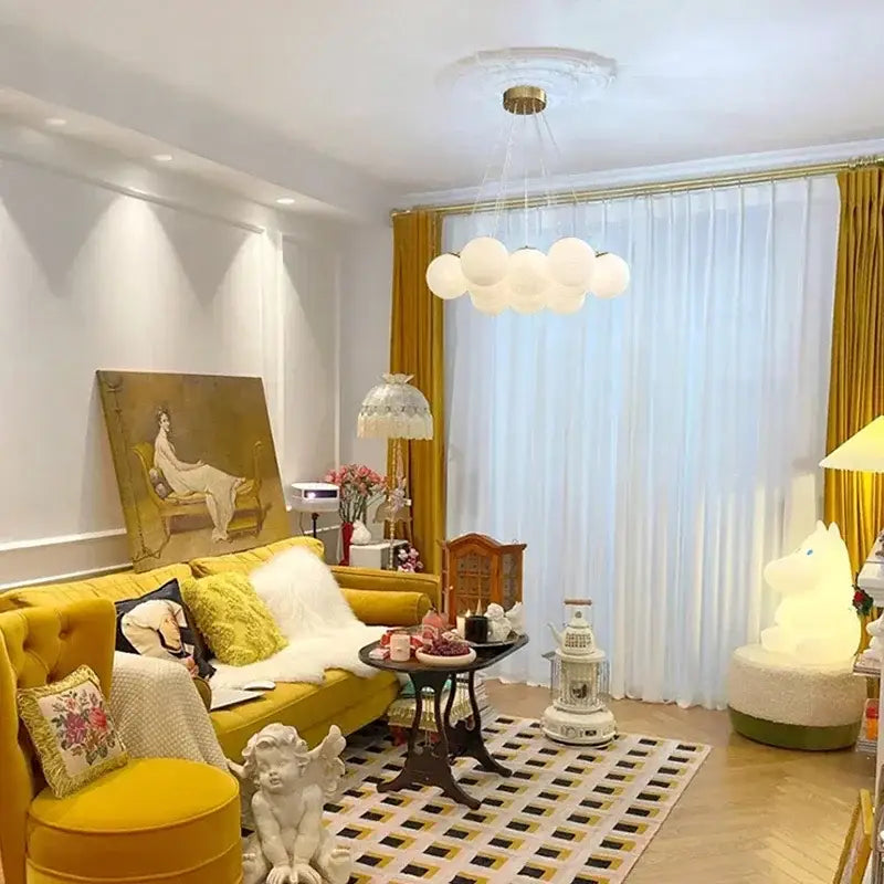 Yellow tufted sofa with plush white fur throw and patterned pillows beneath decorbites glass ball ceiling pendant lights