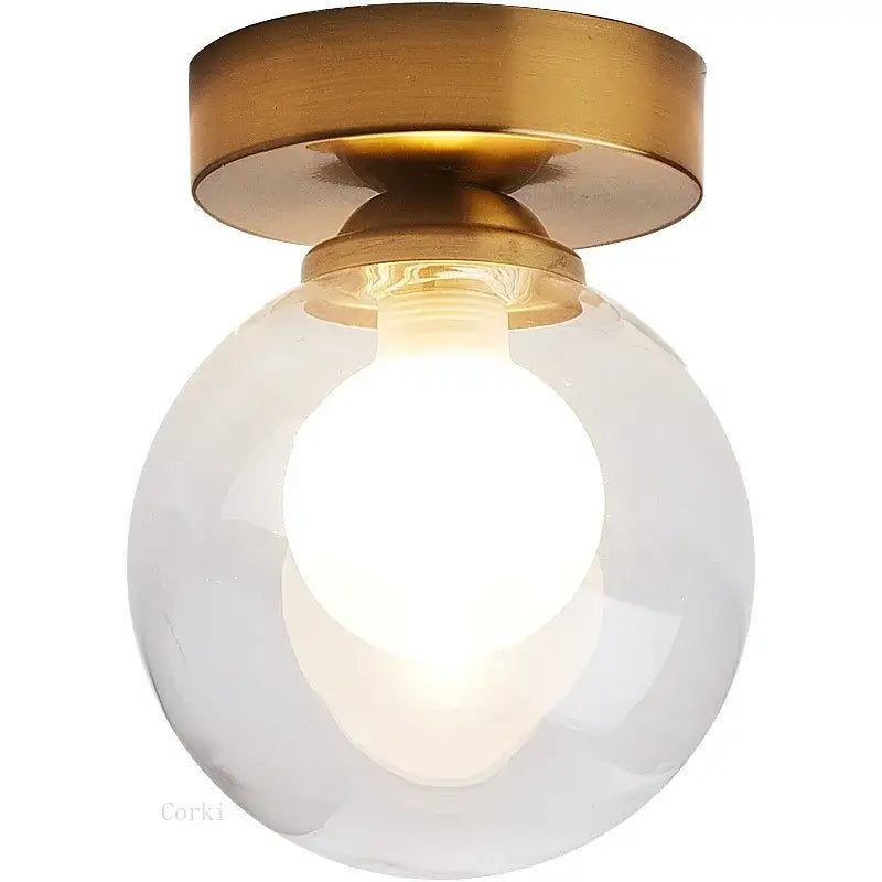 A sleek brass-finished decorbites glass ball ceiling light with a clear glass globe housing an illuminated bulb