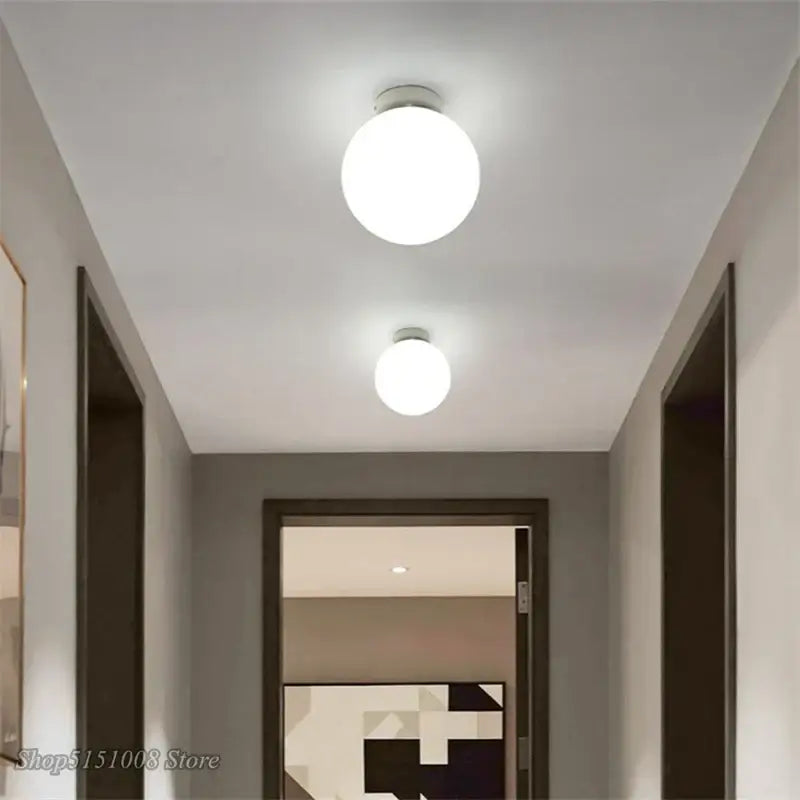 Two round white decorbites glass ball ceiling lights with sleek metallic bases illuminate a modern hallway