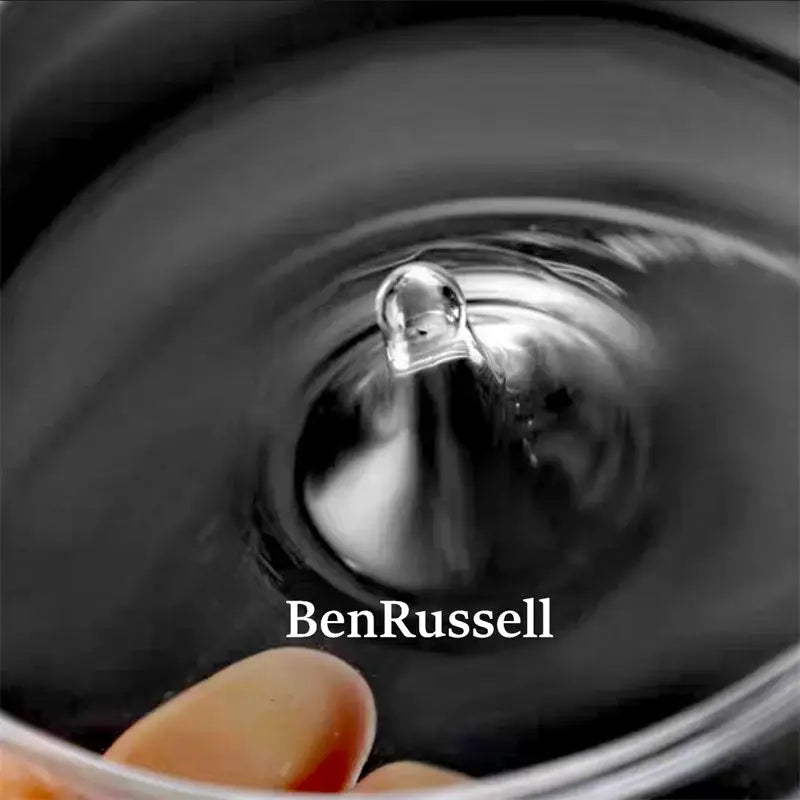 A clear spherical water droplet suspended above a dark liquid surface in the DecorBites™ glass bottle terrarium kit using micro landscape glass