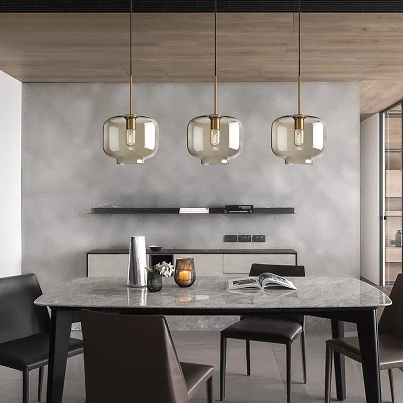 Three modern DecorBites™ glass pendant lights with smoked glass globes and brass accents above dining table
