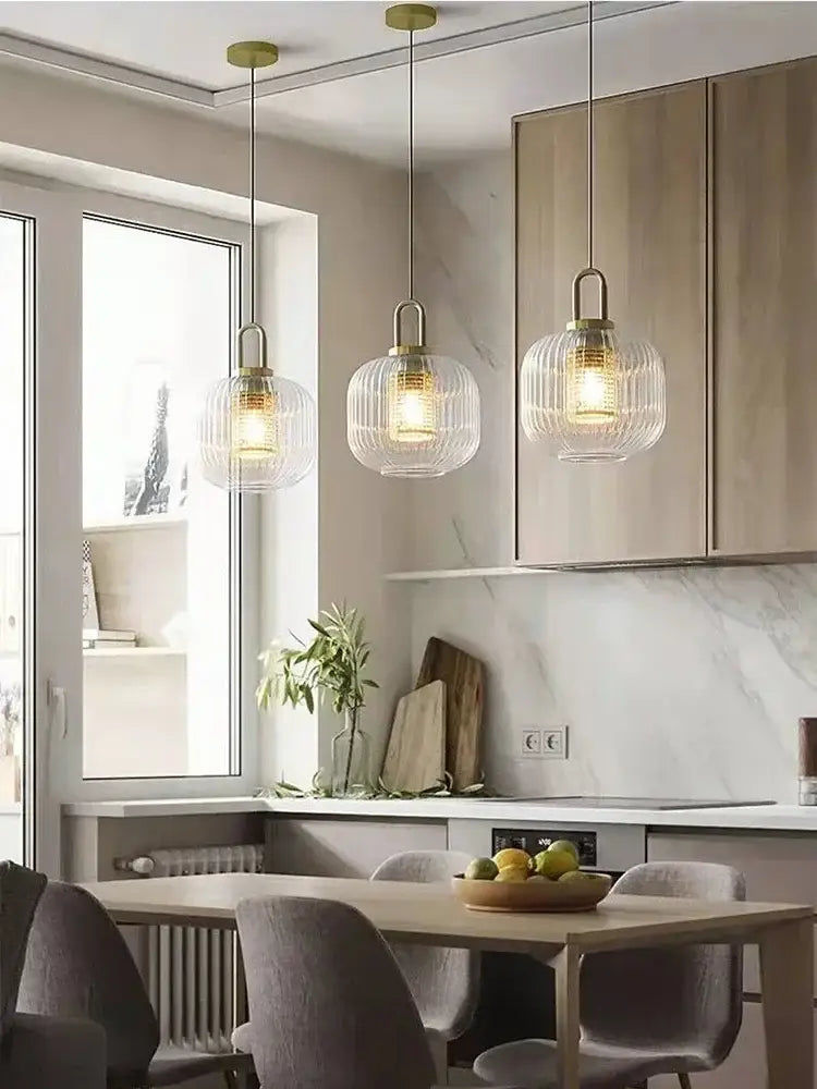 Three elegant brass decorbites glass stripe pendant lights with ribbed shades hang over a dining room table