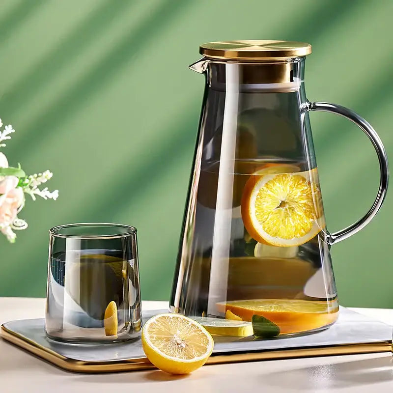 Clear glass tea jug with gold-toned lid and handle filled with water and orange slices from decorbites water kettle set