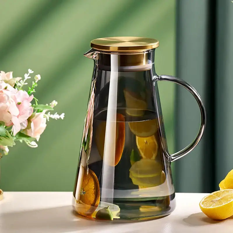 Clear glass tea jug with gold-toned lid and handle filled with citrus water from DecorBites water kettle set