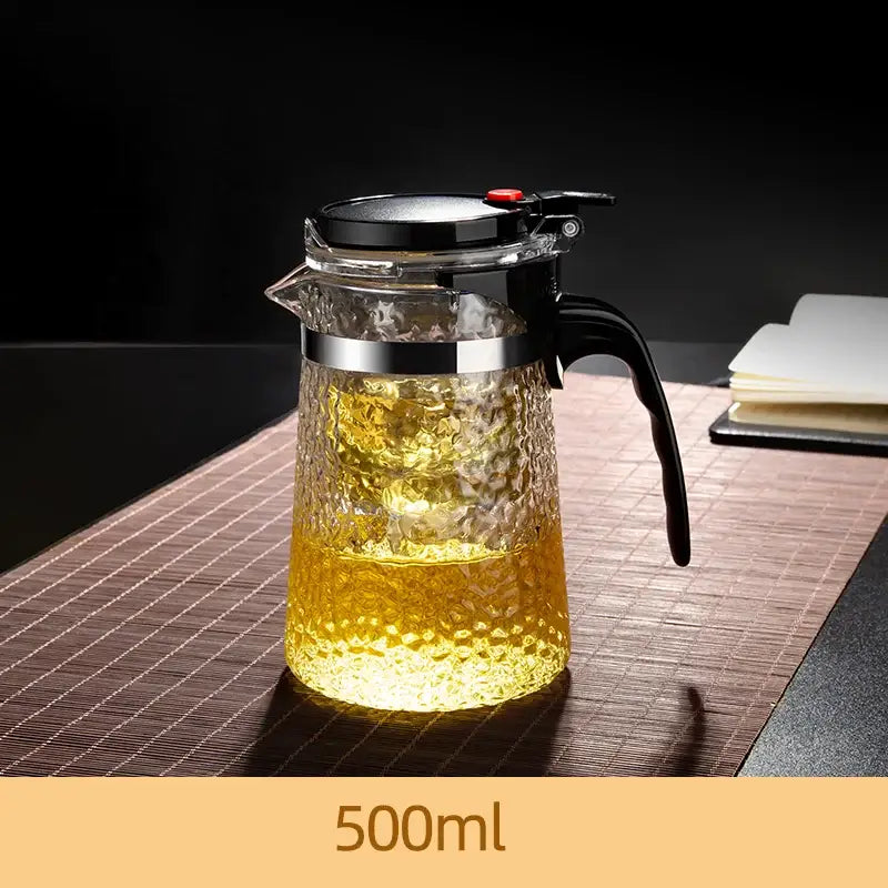 Decorbites glass tea maker with clear textured glass, black handle, silver rim, and black lid with red button for brewing tea