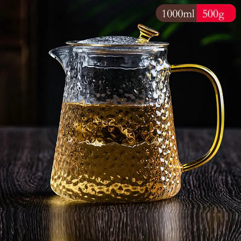 Clear glass tea pot set with hammered texture and gold-toned handle filled with golden tea for kung fu brewing