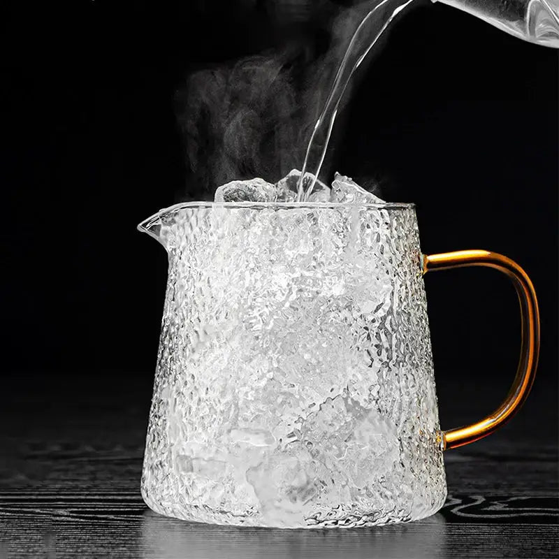 Clear textured glass tea pot set with gold-toned handle filled with ice and hot water steaming for brewing