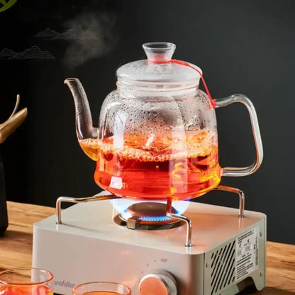 Decorbites™ glass tea pot set with red string handle filled with steaming orange tea for high quality brewing