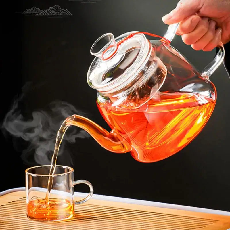 DecorBites™ glass tea pot set with clear glass kettle and lid pouring steaming amber tea into transparent cup