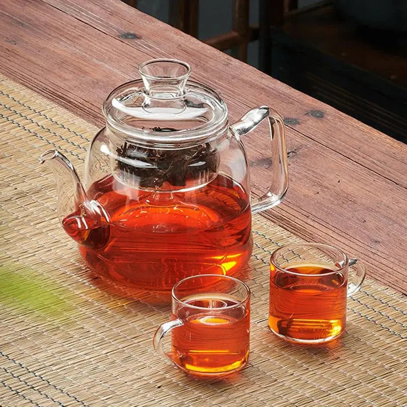 DecorBites™ glass tea pot set with built-in strainer filled with amber tea and dark leaves in clear glass pot