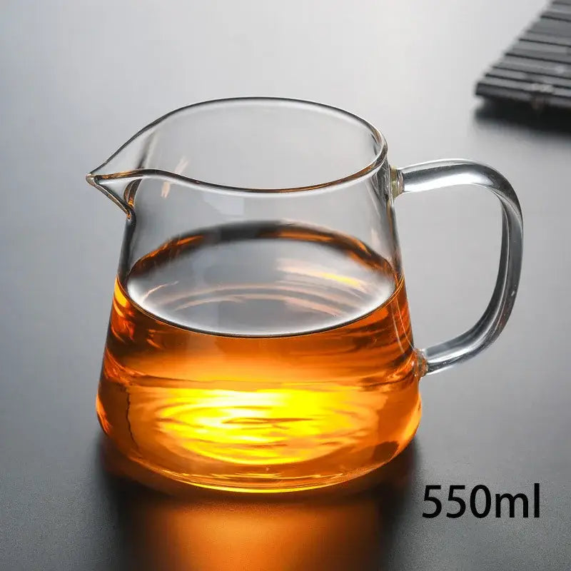 Clear glass tea pot from DecorBites™ tea pot set with curved handle and spout filled with amber-colored tea