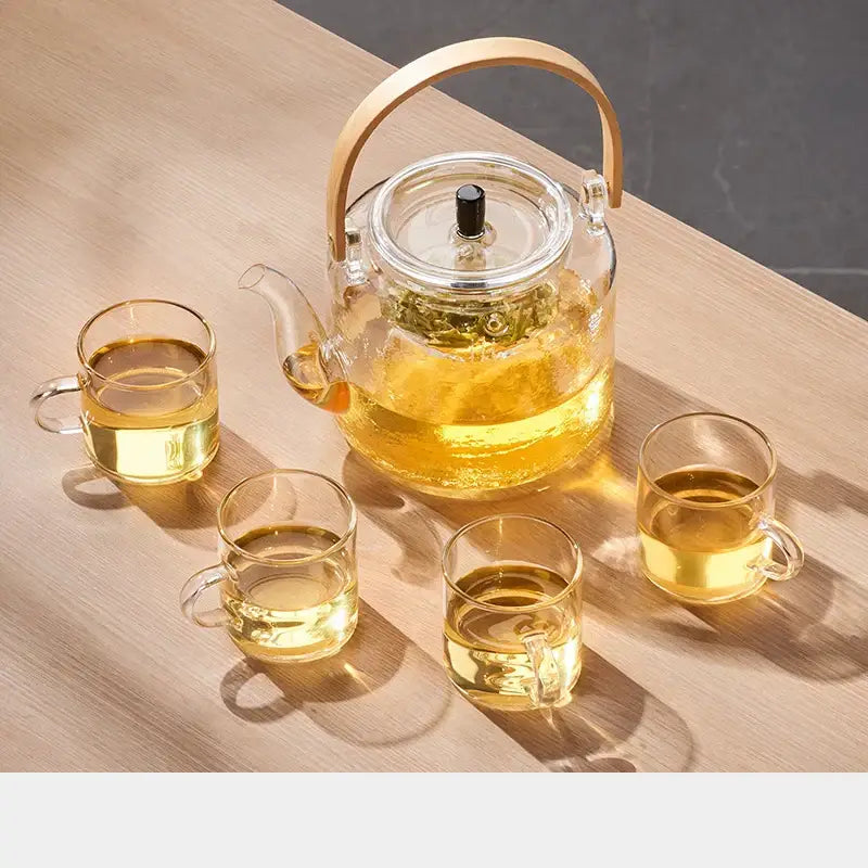 Clear glass decorbites glass tea pot with bamboo handle black lid knob and four matching cups filled with golden tea