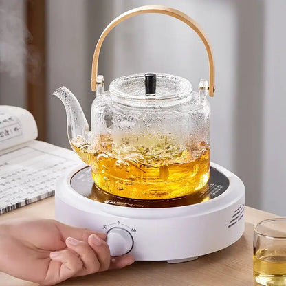 Clear decorbites glass tea pot with bamboo handle black lid on white electric heating base for brewing tea