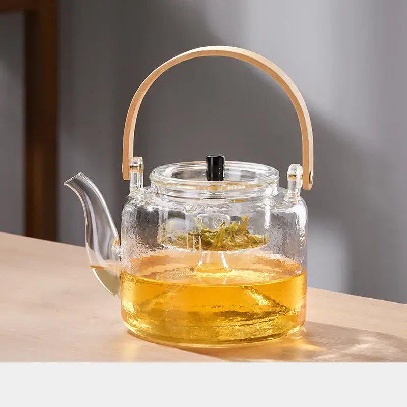 Decorbites glass tea pot with bamboo handle and double filter liner filled with golden tea in clear glass