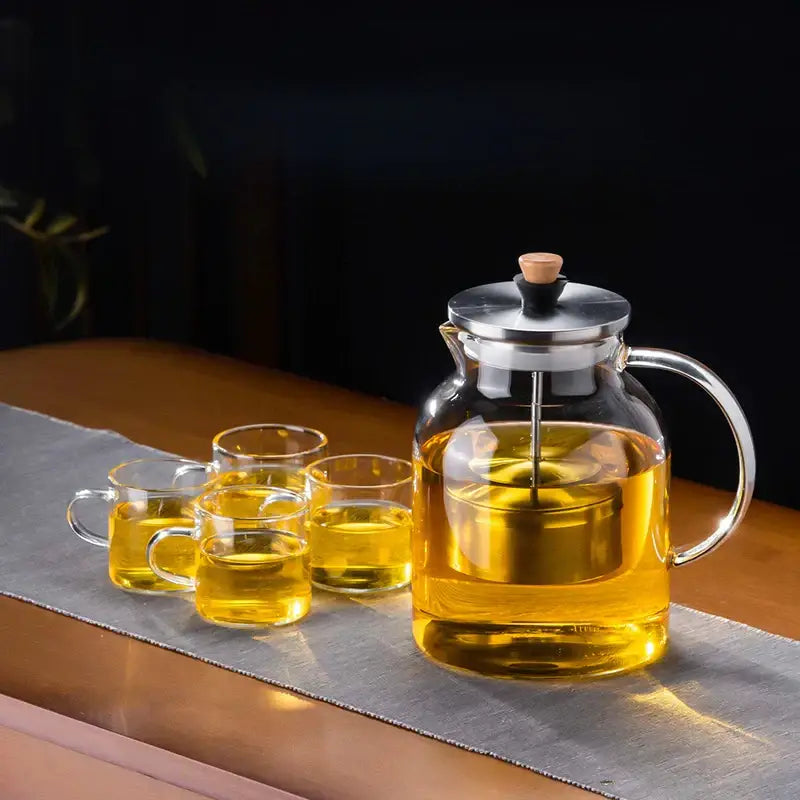 Decorbites glass tea pot with stainless steel lid and handle filled with golden herbal tea in clear glass kettle