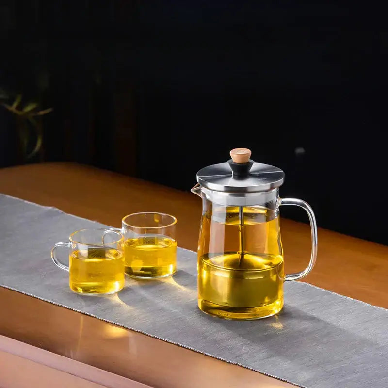 DecorBites glass tea pot with clear glass body, stainless steel lid, wooden knob, and golden tea inside
